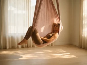 Vrouw in rustgevende houding in een roze aerial yoga hangmat, warm zonlicht filtert door de stof in een minimalistische studio.