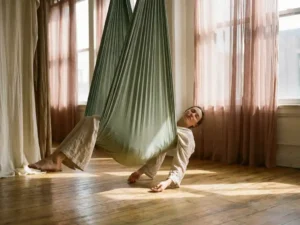 Persoon in rustgevende lighouding in een zijden aerial hammock, verlicht door warm middagzonlicht in een studio met houten vloeren.
